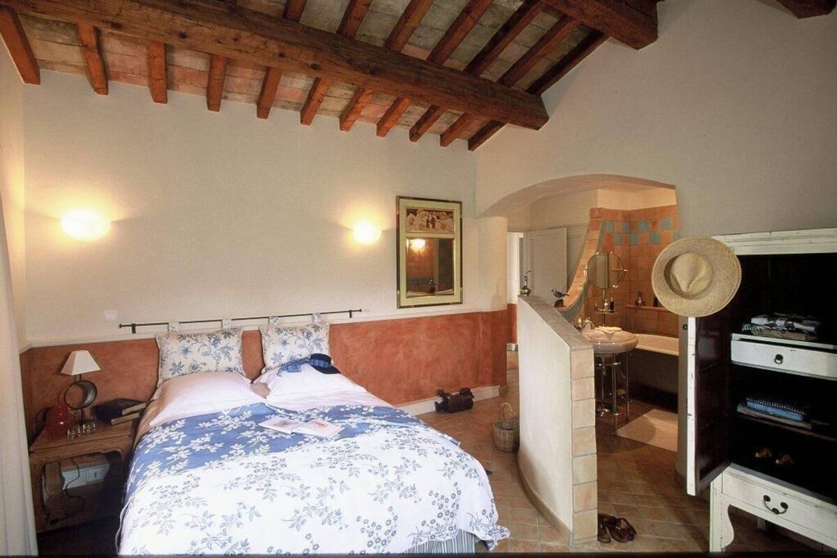 Une chambre à coucher comprenant un lit, une table de chevet, une lampe, ainsi qu’une salle de bain avec un lavabo, un miroir et un porte-serviettes.