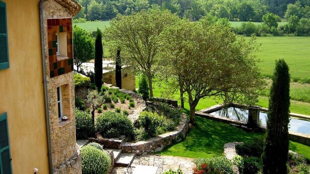 A yellow building with a stone facade, a circular stone garden, and a pond. - Une Campagne en Provence (Bras)