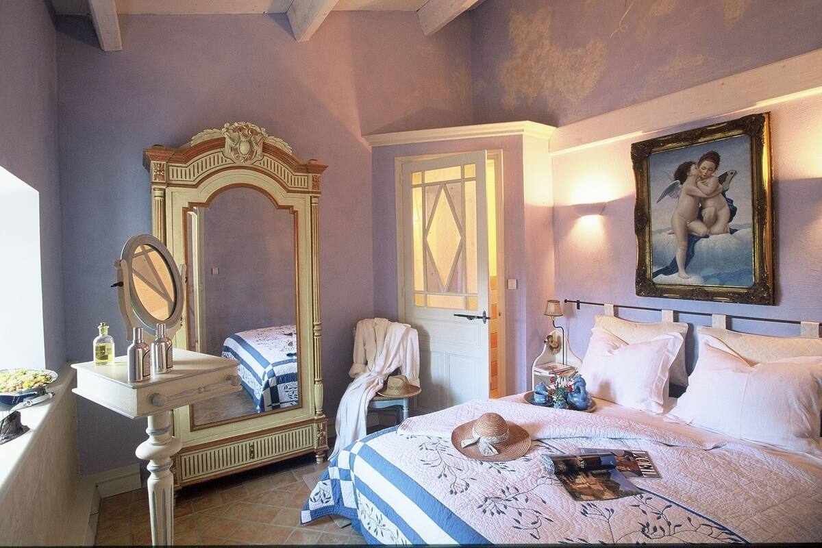 Une chambre avec un grand miroir, un lit recouvert d’une courtepointe à rayures bleues et blanches, une porte blanche et un tableau accroché au mur.