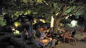 An outdoor dining area with tables and chairs under a large tree, surrounded by stone walls and greenery. - Une Campagne en Provence (Bras)