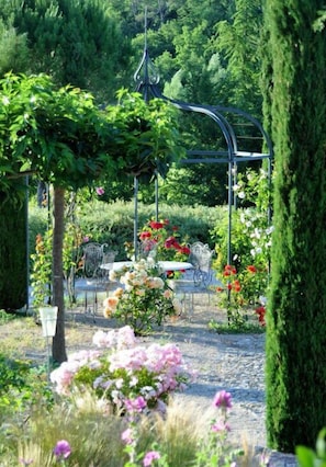 Un jardín con un porche metálico, una mesa y sillas.