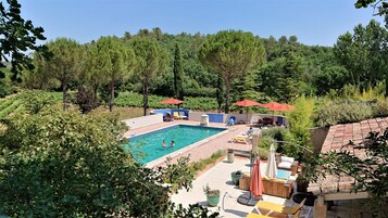 Una piscina con sillas de descanso y sombrillas, rodeada de árboles y un viñedo.
