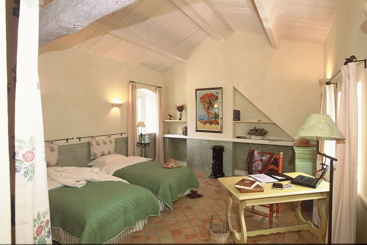 Une chambre avec deux lits, un bureau avec un ordinateur portable, une lampe et un tableau au mur.