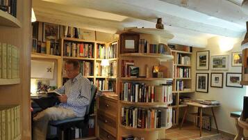 Una habitación acogedora con una estantería de madera llena de libros, un escritorio con silla y una mesita con lámpara.