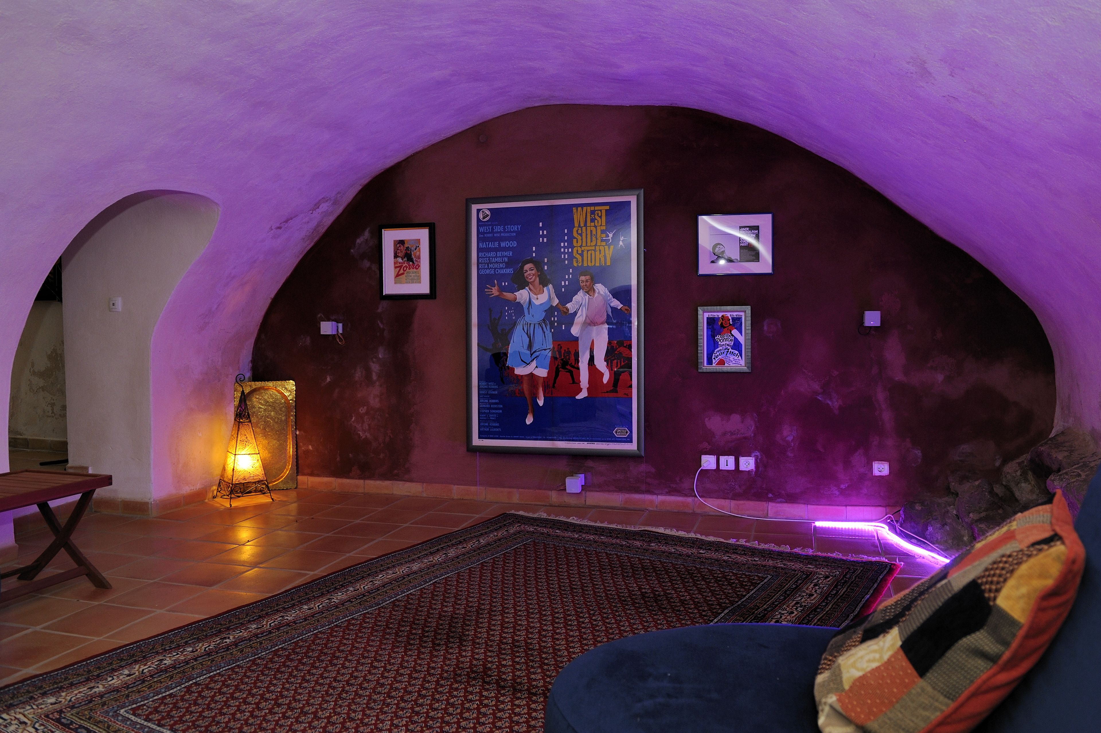 A cozy room with a large poster of 'West Side Story' on the wall, a patterned rug, and a bench.