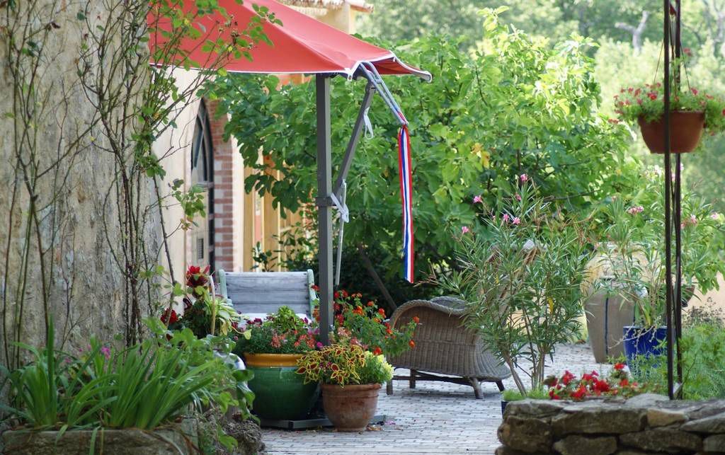 A garden with a red umbrella, potted plants, and a wicker chair.