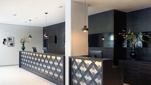 Un espace d’accueil moderne avec un comptoir aux motifs géométriques, des panneaux de bois foncé et un design minimaliste.