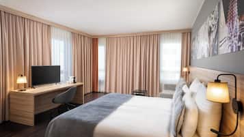 Quarto de hotel com cama, escrivaninha, cadeira, televisão e obras de arte na parede.