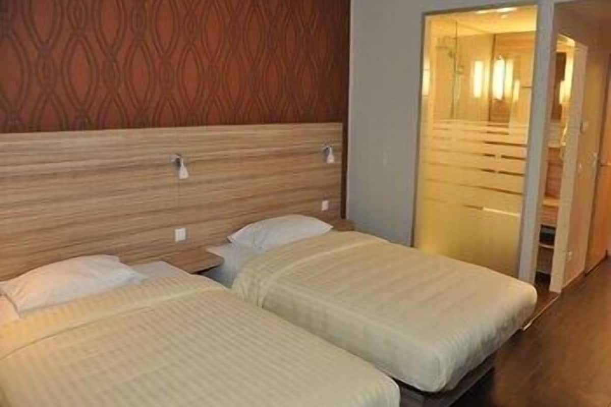 Ein Hotelzimmer mit zwei Betten, einem Holz-Kopfteil und einem Spiegel.