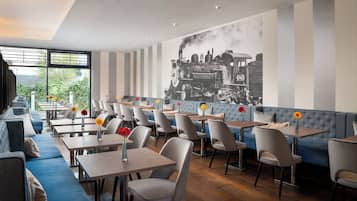 Ein Restaurant mit modernem Interieur, das sich durch gestreifte Wände, ein großes Schwarz-Weiß-Wandgemälde mit einem Zugmotiv und eine Mischung aus Sitzgelegenheiten wie Tische und Sofas auszeichnet.