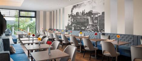 A restaurant with a modern interior, featuring striped walls, a large black and white train mural, and a mix of seating options including tables and sofas.