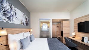 Une chambre d’hôtel moderne, dotée d’un grand lit, d’un bureau, d’une chaise, d’un téléviseur à écran plat et d’un grand tableau accroché au mur.