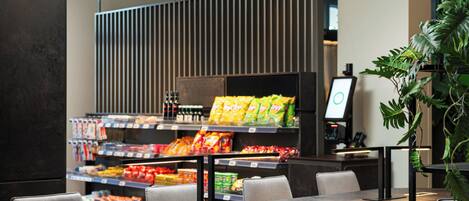 A modern restaurant with a counter displaying snacks and beverages, seating area with tables and chairs, and a large potted plant.