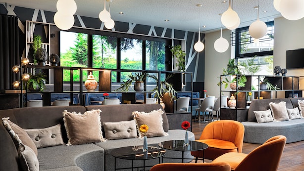 Un espace de détente moderne, doté de canapés, de fauteuils et d’une table basse. De grandes fenêtres offrent une vue sur la verdure environnante.