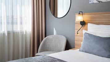 A hotel room with a bed, a chair, a round mirror, and a wall-mounted lamp.
