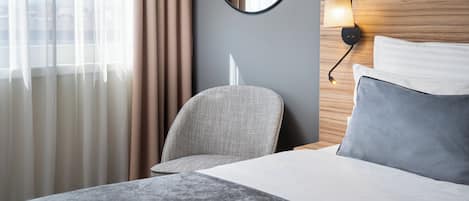 A hotel room with a bed, a chair, a round mirror, and a wall-mounted lamp.