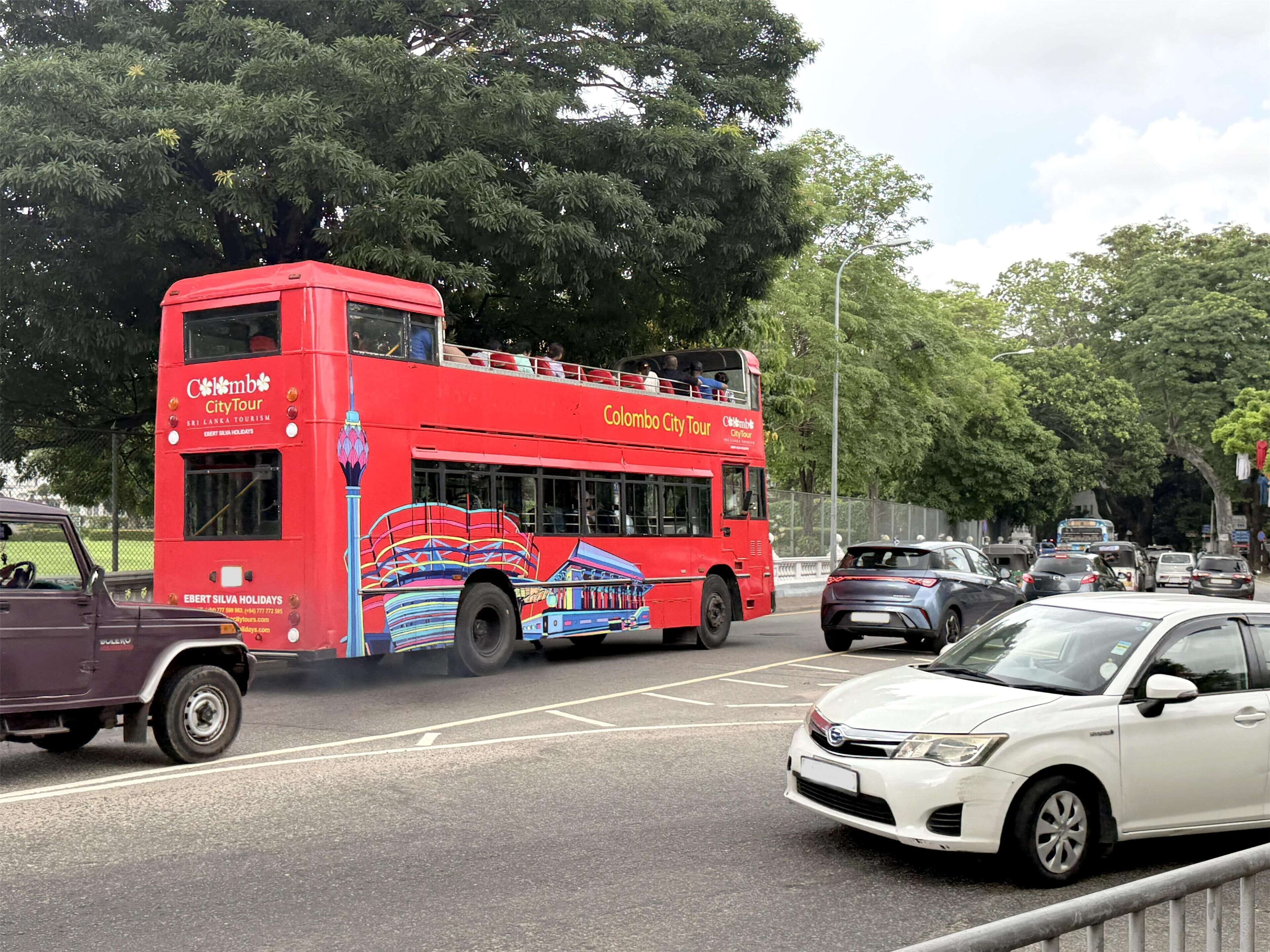 Un autobus a due piani rosso con la scritta 'Colombo City Tour' sul lato, parcheggiato in una strada trafficata.