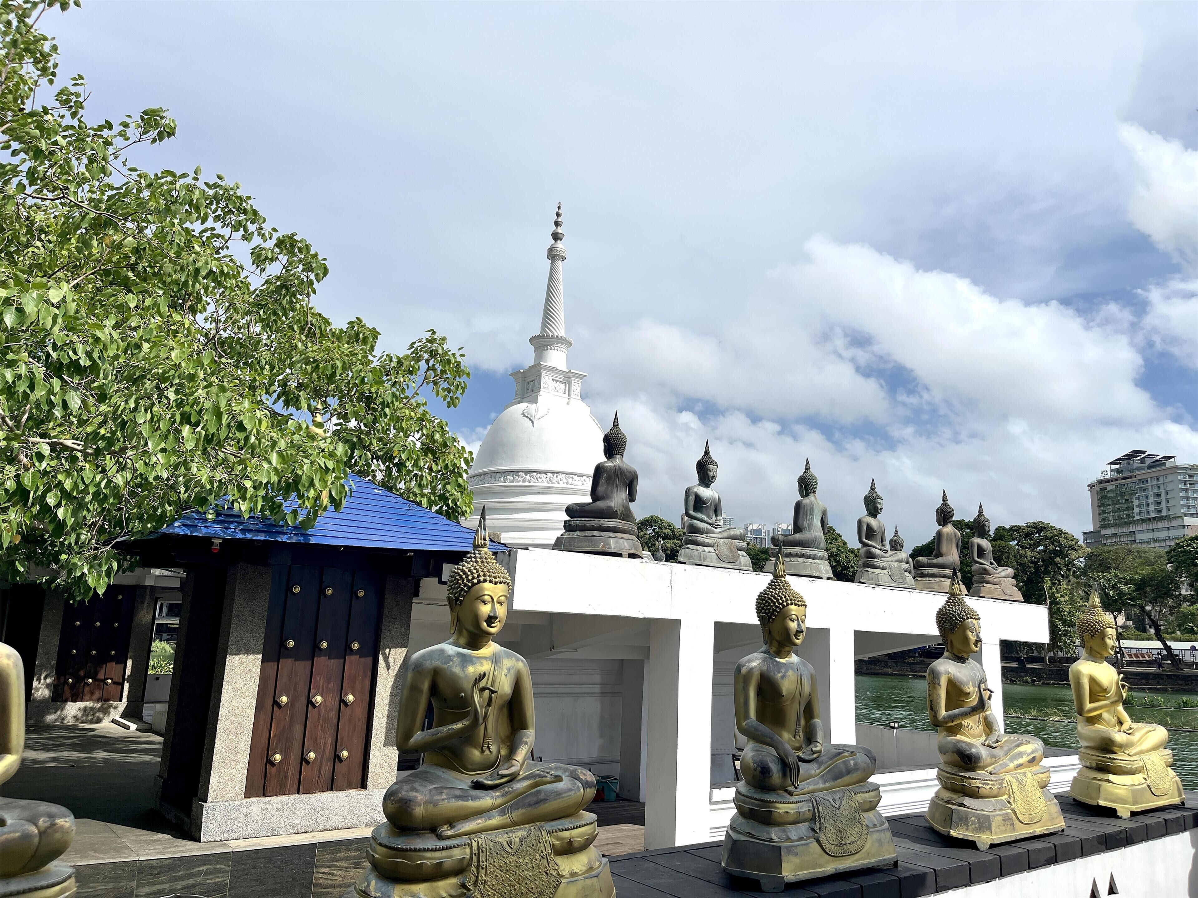 A row of seated Buddha statues in a temple courtyard with a white pagoda in the background.