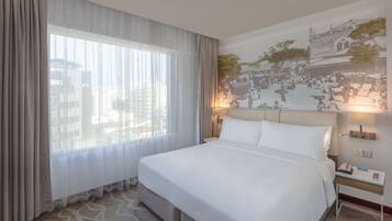 Et hotelværelse med en stor seng, et natbord med lampe, og et vægmaleri.