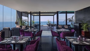 Un restaurante con mesas y sillas, vistas al océano y ventanas amplias.