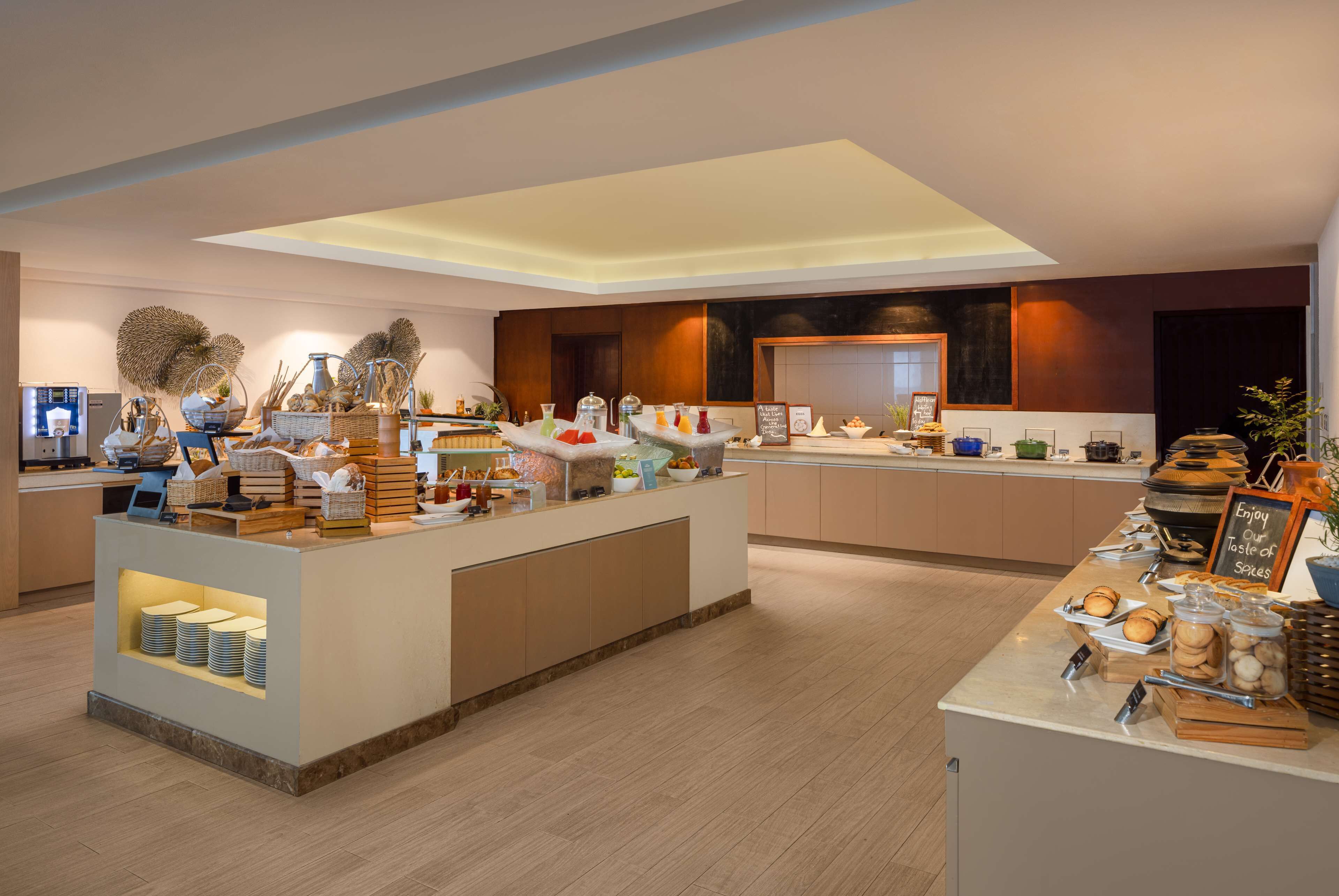 A modern hotel lobby with a central reception desk, a coffee station, and a buffet area.
