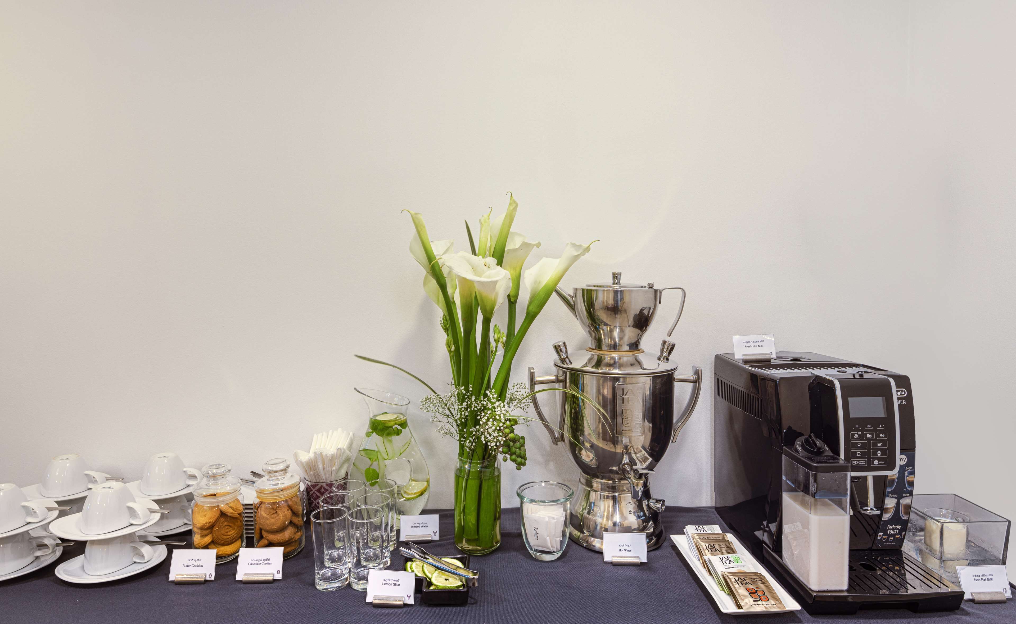 A table with various coffee and tea products, including jars of cookies, a pitcher of water, and a coffee machine.