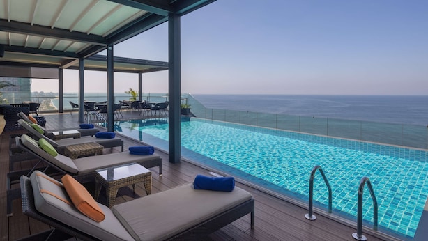 Una piscina infinita en la azotea con sillones de descanso y vista al océano.