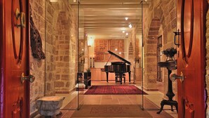A grand hallway with stone walls, a grand piano, and a red carpet leading to a kitchen area. - Kókkini Porta Rossa (Rhodes)