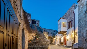 A narrow street with stone buildings, a staircase, and a view of a fortification in the background. - Kókkini Porta Rossa (Rhodes)