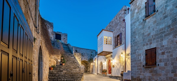 A narrow street with stone buildings, a staircase, and a view of a fortification in the background.