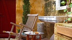 A wooden chair with a metal frame, a small round table with a bowl of food, and a stone wall with a water feature.