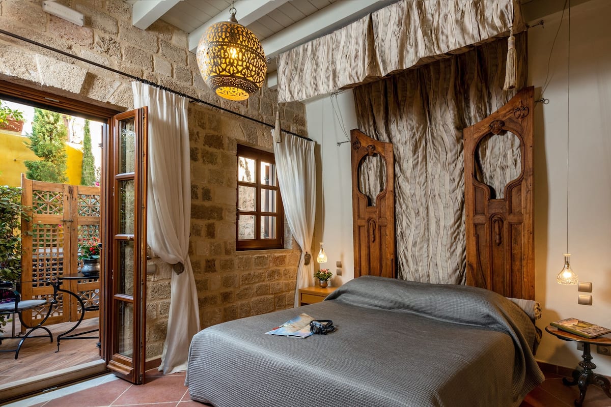 A bedroom with a bed, wooden doors, a window, and a hanging light fixture.