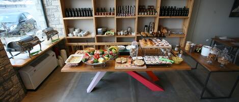 A bakery with a variety of baked goods displayed on tables, a large window with a view of the street, and shelves stocked with jars and bottles.