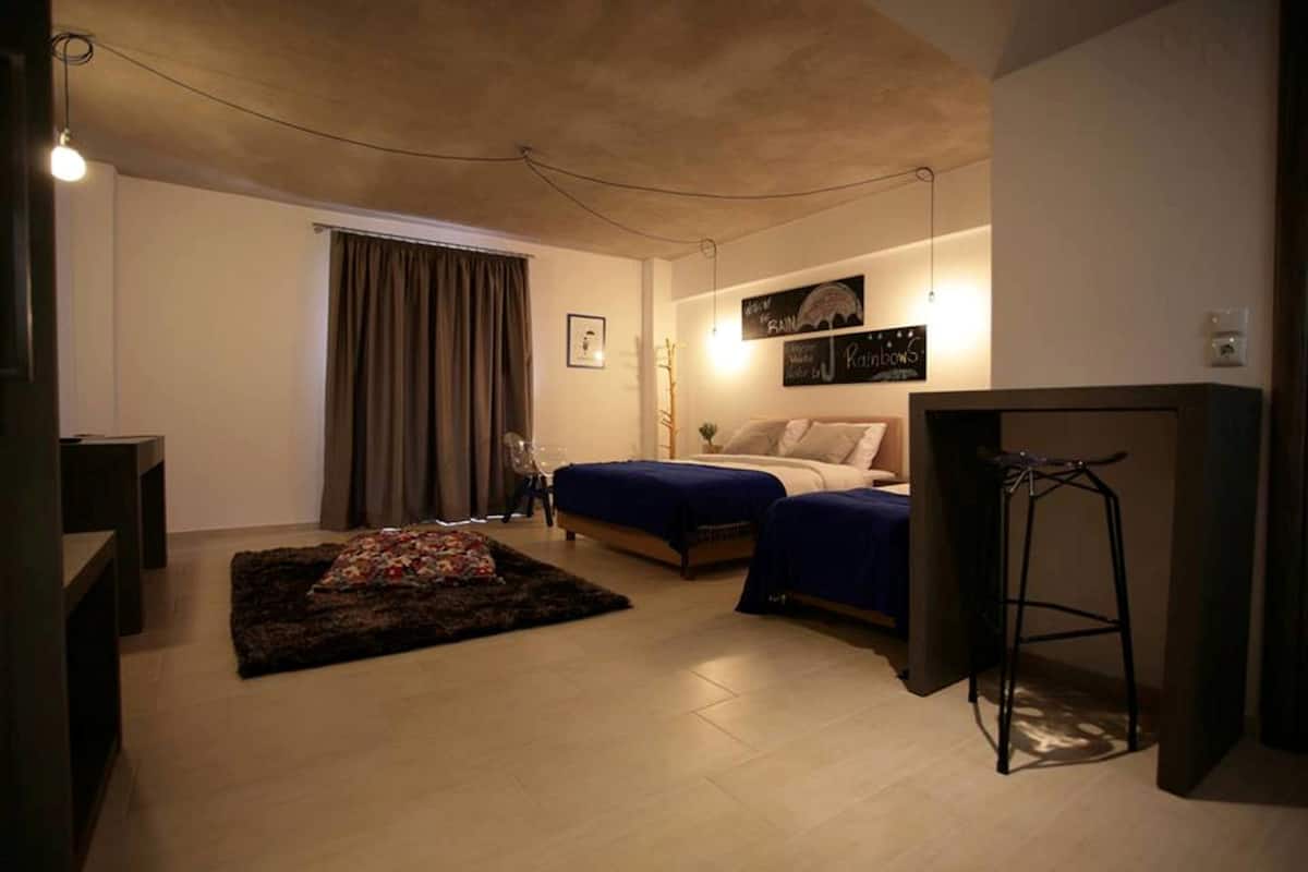 A bedroom with two beds, a desk, a chair, a small rug, and a hanging light fixture.