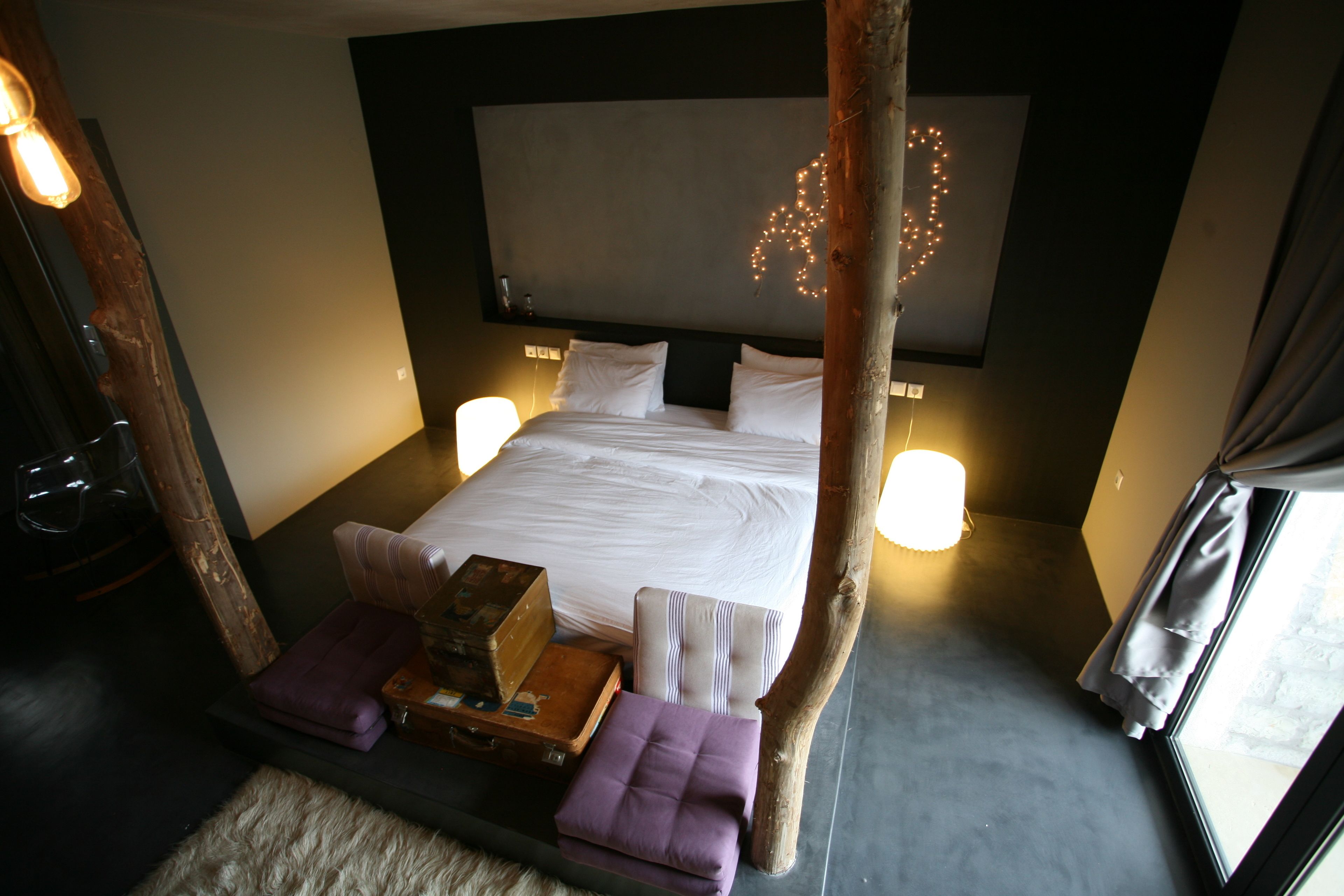 Un dormitorio con una cama grande, lámparas de noche, cabecera de madera y una ventana con cortinas.