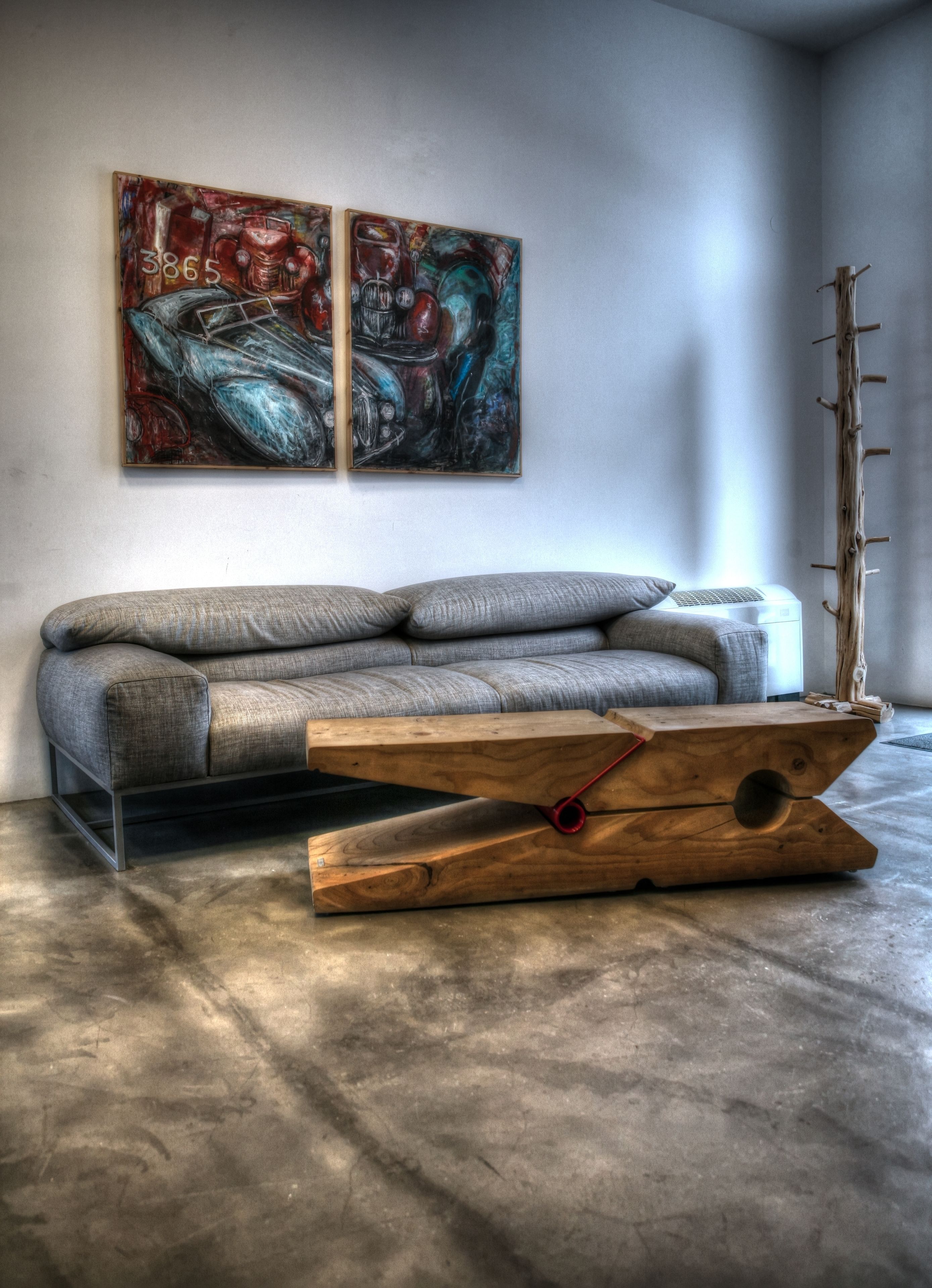Un saló modern amb un sofà gris, dues pintures abstractes i una taula de centre de fusta original.