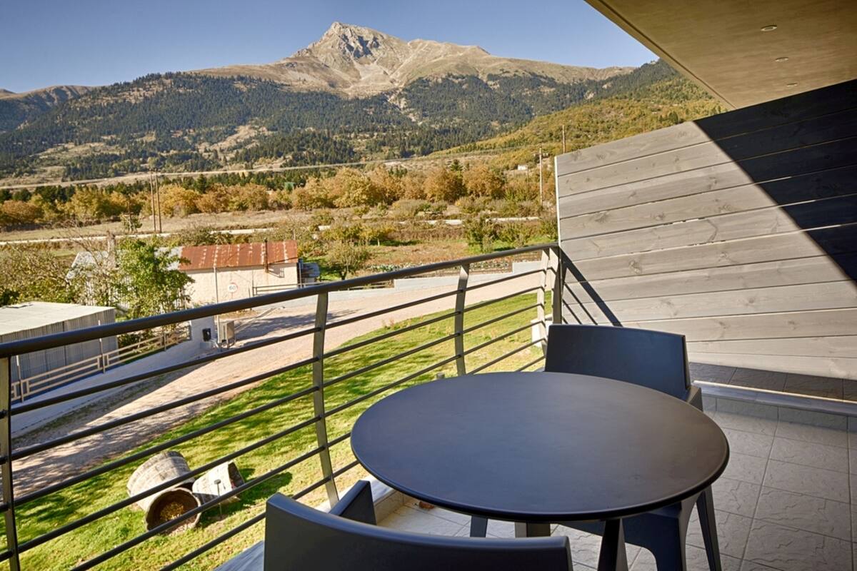 A balcony with a table and chairs, overlooking a mountainous landscape.