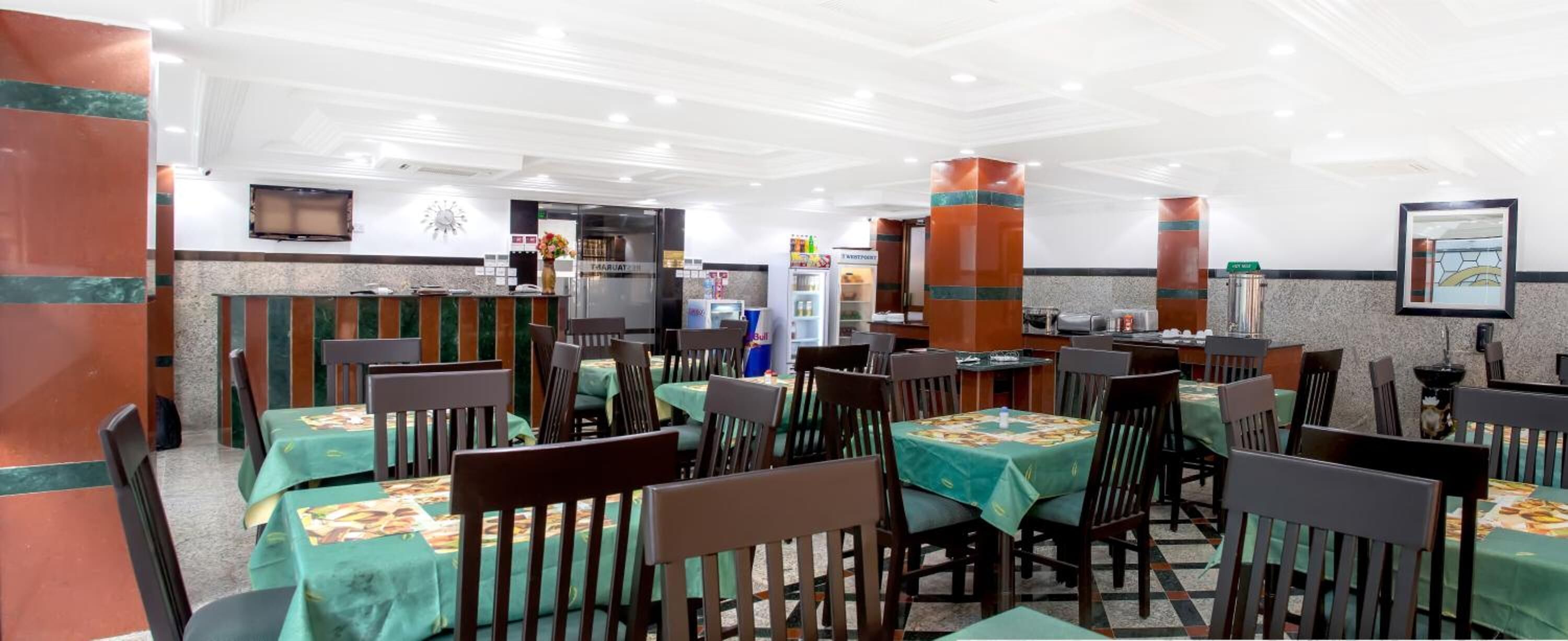 A restaurant with multiple tables and chairs, a counter with a cash register, and a refrigerator.