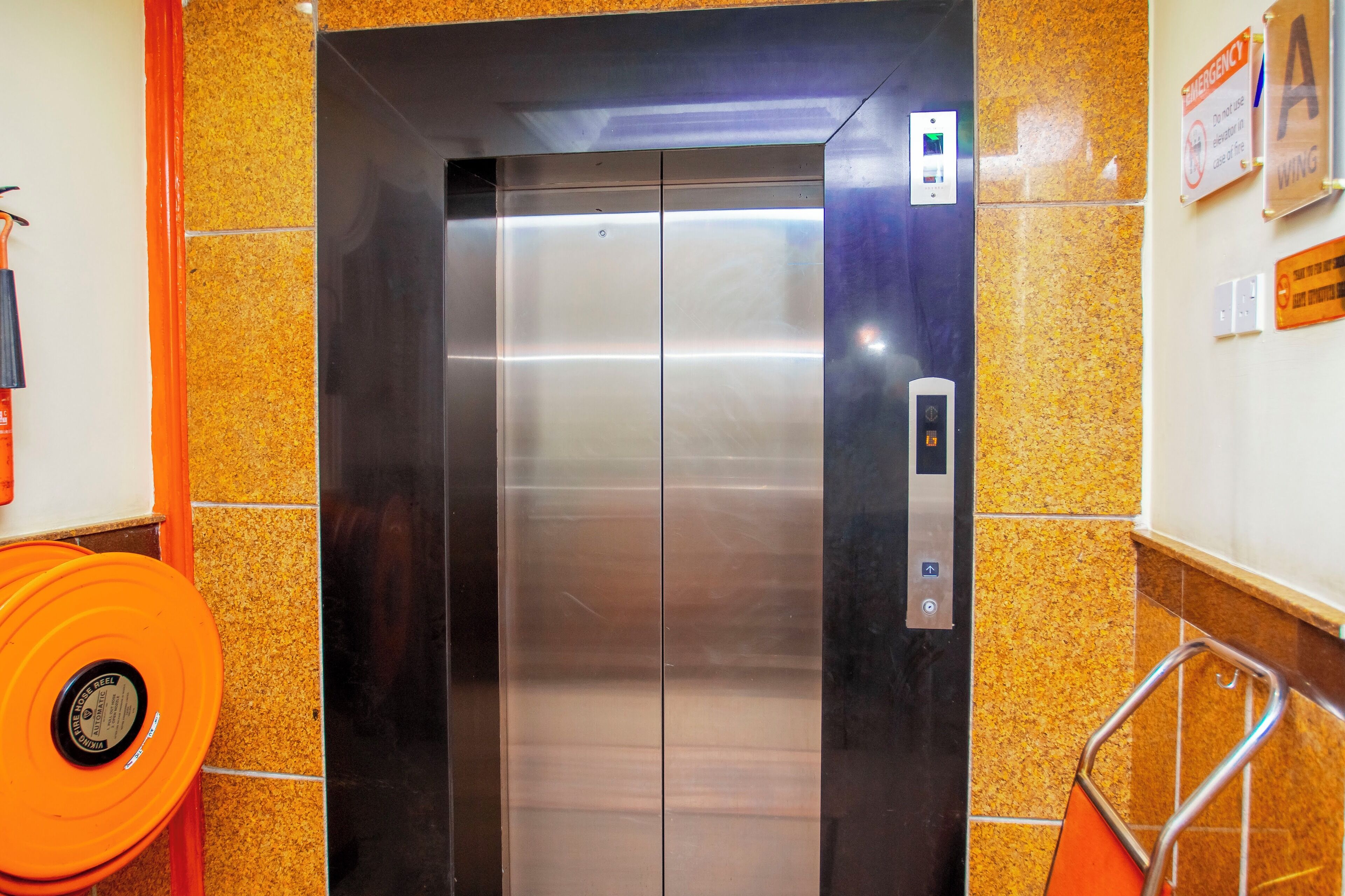An elevator with a metallic finish, emergency signage, and a handrail.
