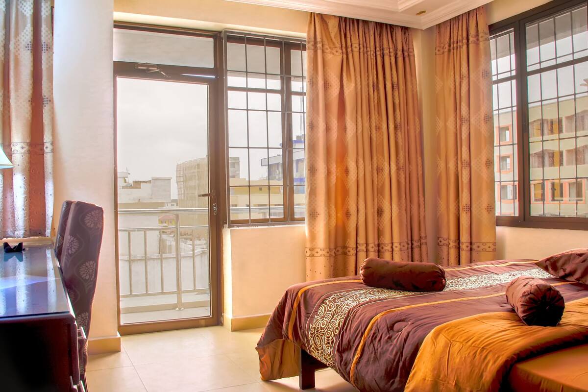 A room with a bed, a desk, and a view through a large window.
