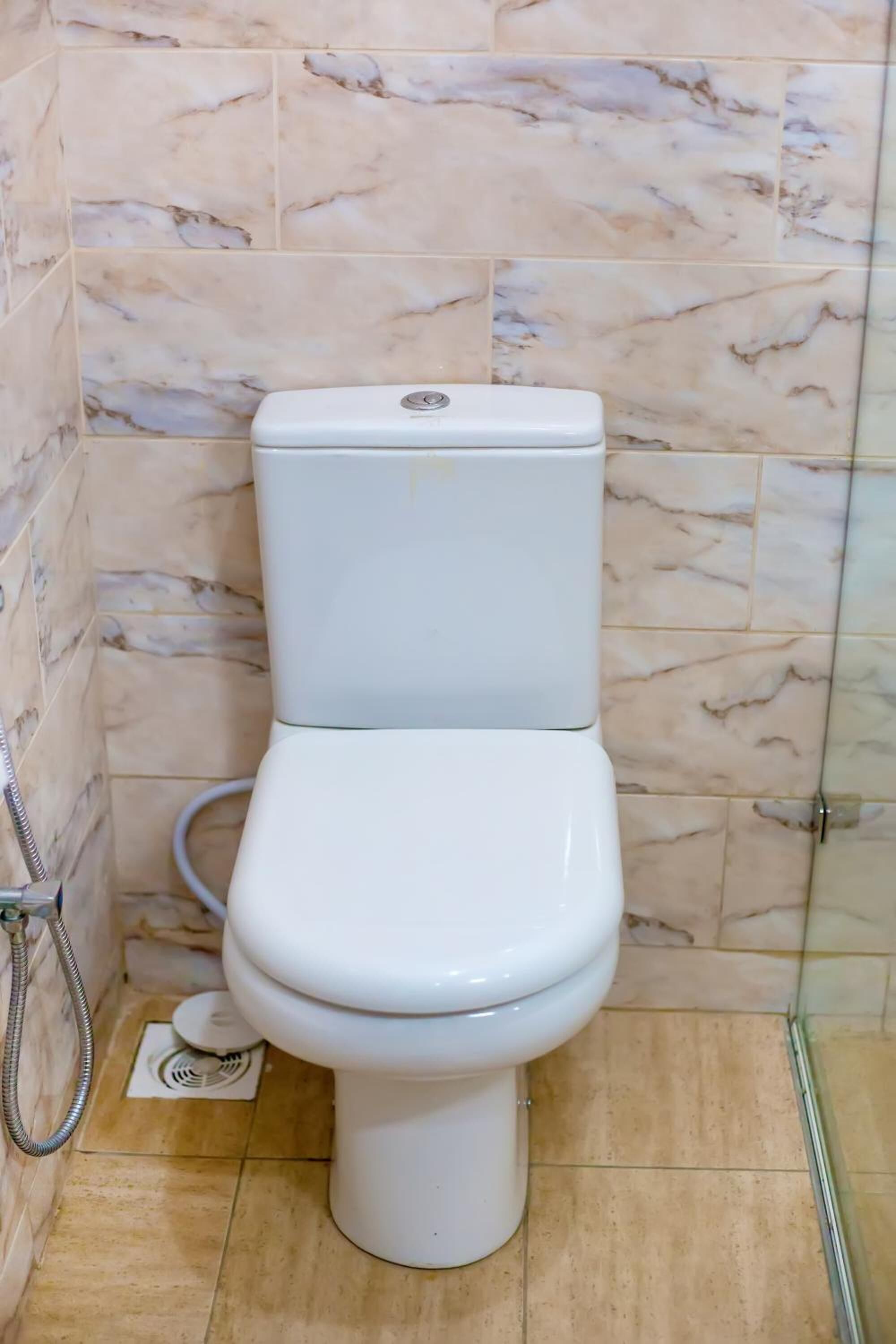 Un inodoro en un baño con baldosas de mármol y cabina de ducha de cristal.