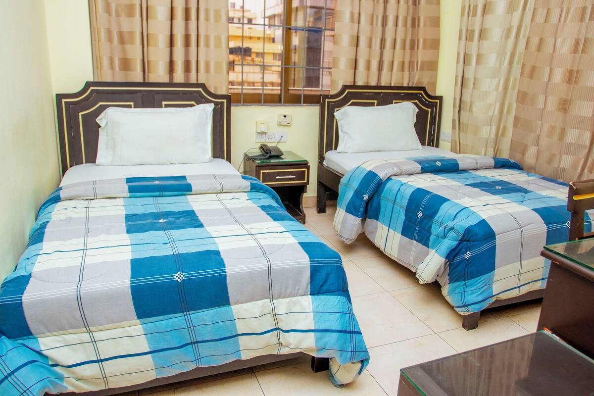 Two single beds with blue and white checkered bedding, a nightstand with a phone, and a window with curtains.