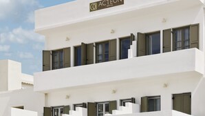 Un hôtel à plusieurs étages, doté d’une façade blanche, de balcons avec des volets verts et surplombant un ciel dégagé.