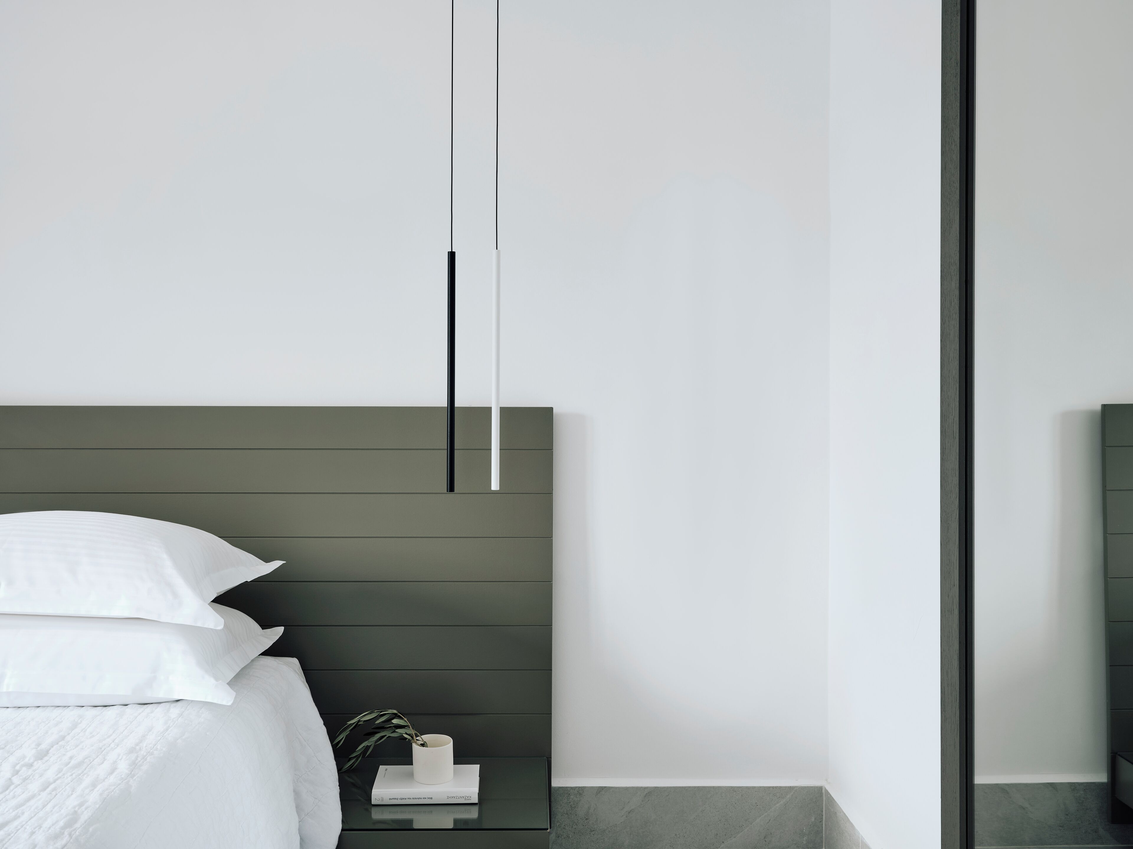 A modern bedroom with a bed, bedside table, and a nightstand with a plant.