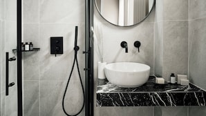 Une salle de bain moderne avec une douche à parois de verre, un miroir rond et un lavabo sur colonne blanc.