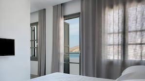 Une chambre d’hôtel moderne dotée d’un grand lit, d’un téléviseur fixé au mur et offrant une vue sur la mer par une fenêtre.