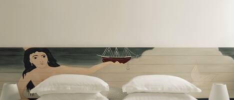 A bedroom with two beds, a mural of a woman and a boat, and a view of the sea.
