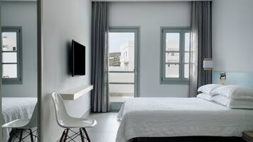 Una moderna camera d'hotel con un letto grande, una sedia bianca, TV a parete e ampie finestre con tende.