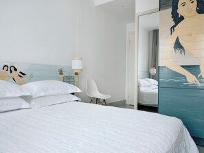 A modern bedroom with a large bed, a white chair, and a wall mural. - Acteon Hotel (Ios)