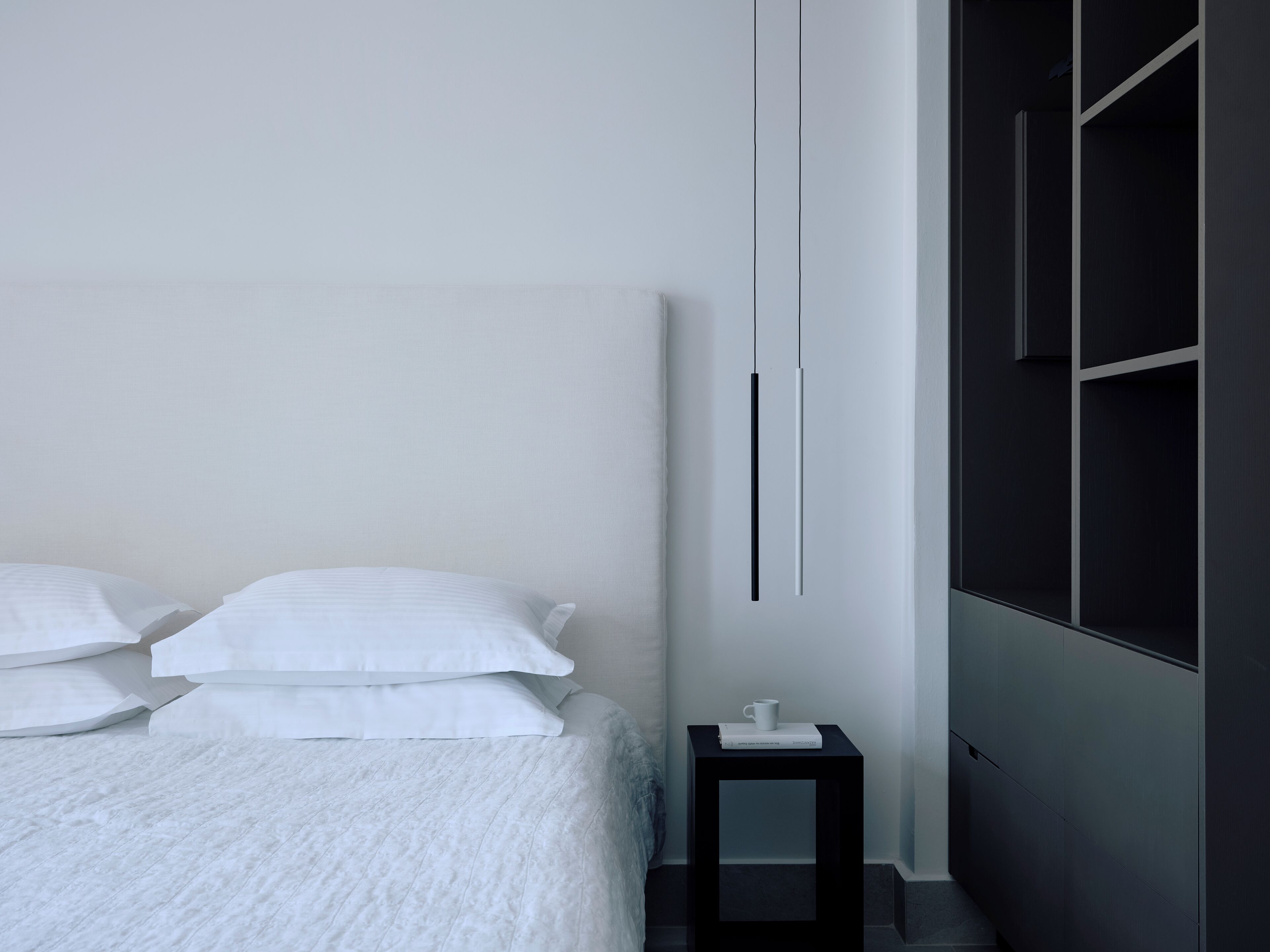 Une chambre moderne avec un grand lit, une table de chevet sur laquelle se trouve une tasse, et une armoire avec un miroir.